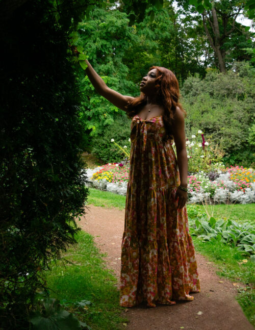 A wooman reaches out for a bush of plants in a park.