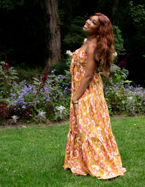 A woman in a floral dress tilts her head in a park.
